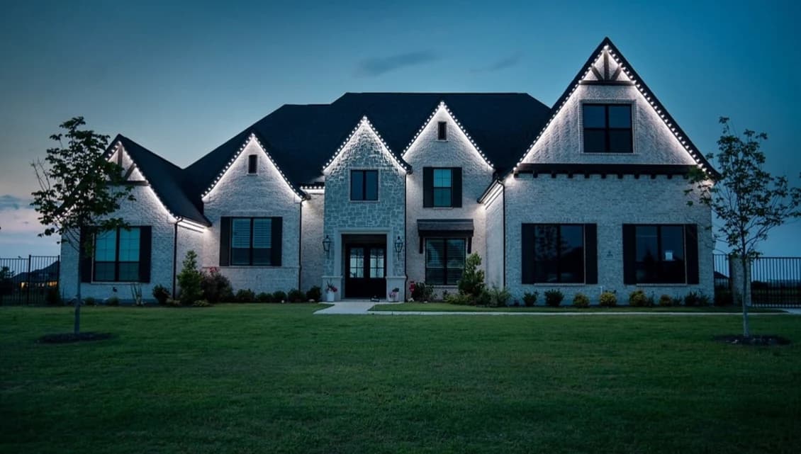 The same home after installation, with white permanent lighting tracing its roofline at dusk.