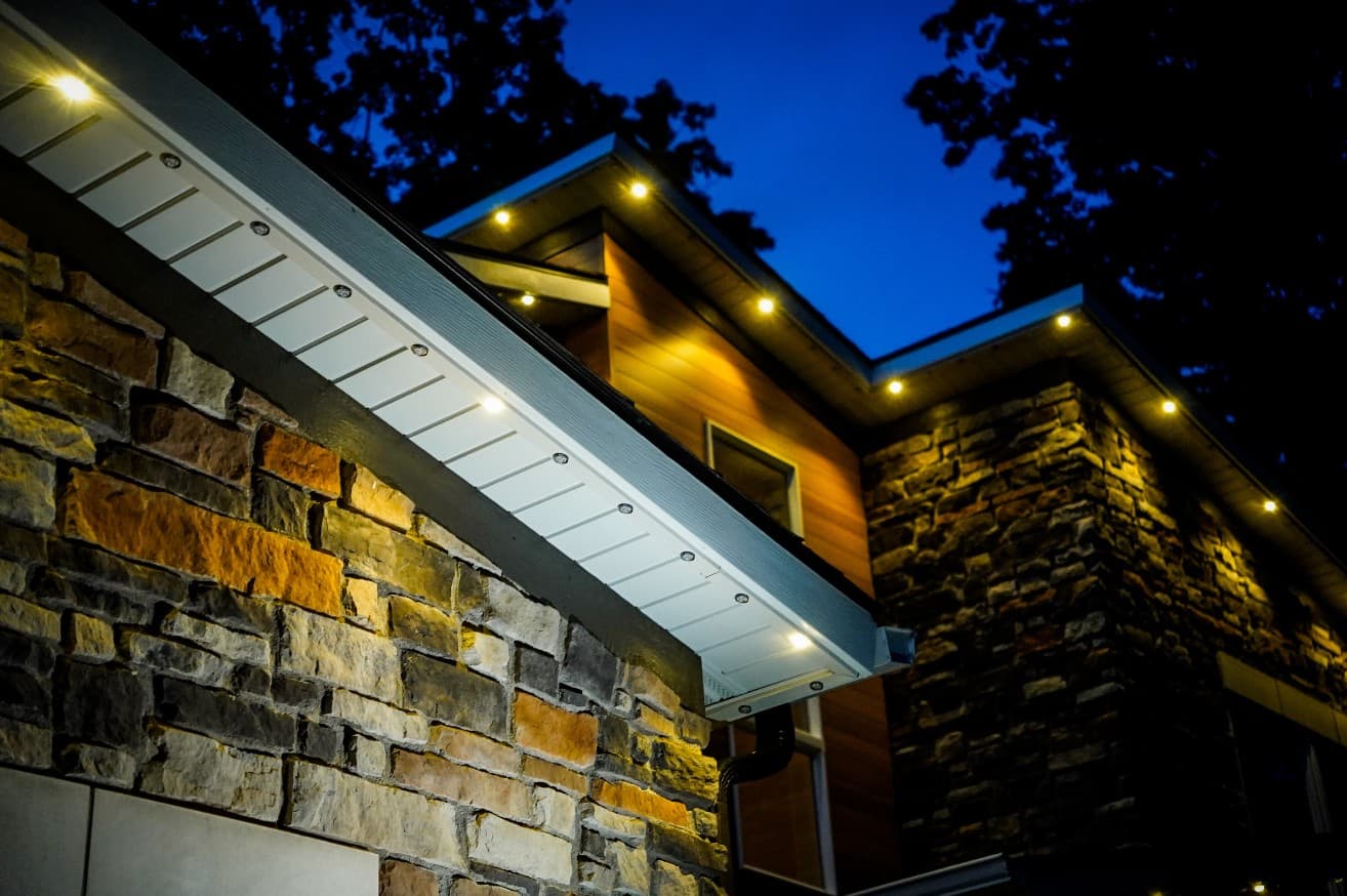 Close view looking up at a white soffit with a color-matched lighting track and warm white lights shining down a stone wall