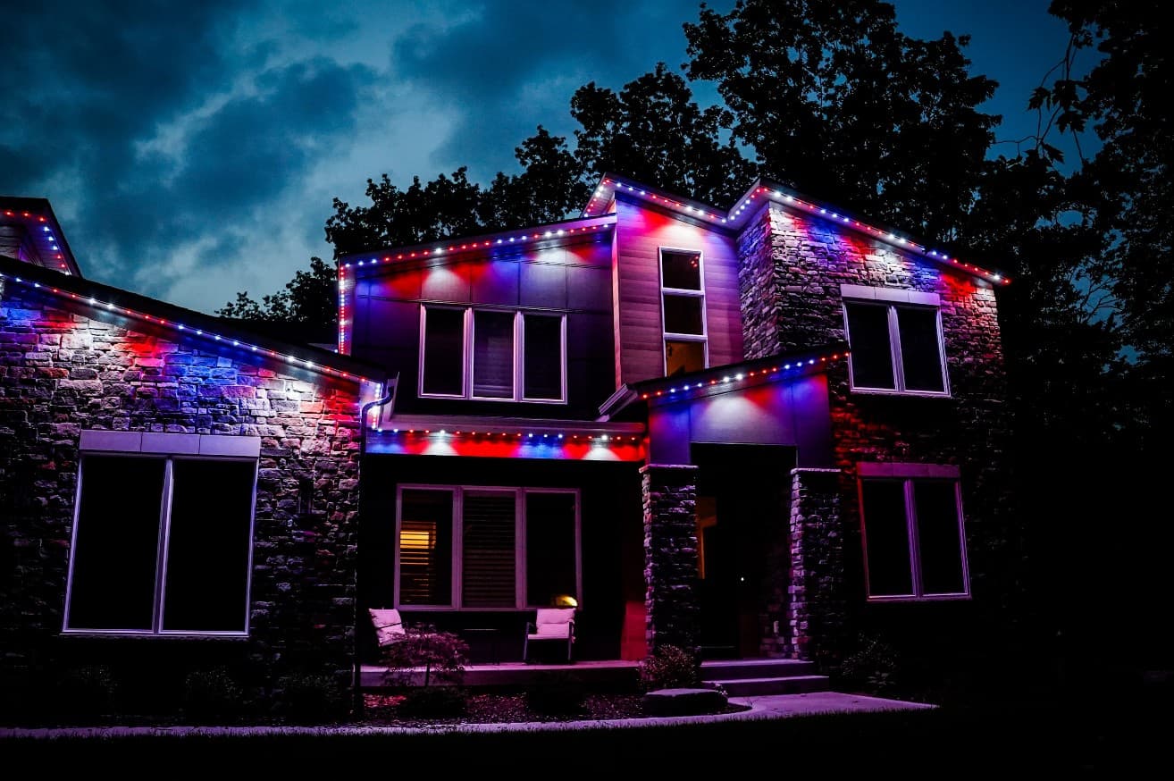 Two-story stone home at night with the roofline lit in alternating red, white, and blue lights
